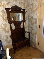 Full front view of dark stained oak hall tree showing carved crest, mirror, armrests, bench base