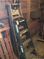 Photo showing two ladders leaning against a wooden wall, black resin Maximum ladder in front, wooden ladder behind