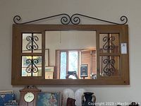 Front view of wood framed mirror with metal scroll details and central rectangular mirror with side panels.