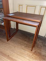 Pair of wood nesting tables showing the larger table on top with the smaller table nested underneath, placed on a wood floor in front of a door.