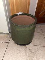 Full view of green glazed planter placed on tiled floor next to wood walls and cabinetry