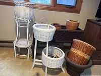Wide view of multiple wicker planters, baskets, and ceramic pots grouped together near a window indoors.