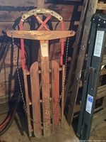 Full view of the vintage wooden sleigh standing against a wall, showing the metal runners and wooden slats with Spartan branding visible on the front slat.