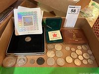 Photo of a collection including multiple Canadian silver dollars, 50 cent coins, commemorative coins, and postage stamp sheets in a cardboard container.
