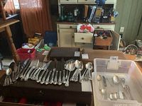 Full spread of sterling flatware on table alongside plastic bin of silverplated pieces
