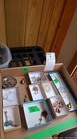 Overview of cardboard box containing small trays of assorted sterling silver jewelry pieces.