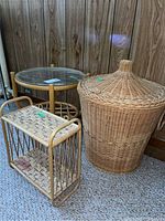 Three items displayed together: bamboo side table with glass top and lower shelf, large woven basket with conical lid, and small woven shelf.