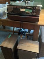Photo of Dual 1226 turntable with clear dust cover on a wood table, with speakers beneath the table.