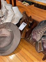 Four pairs of vintage ice skates, brown and white, alongside a worn Stetson hat with a Boy Scout badge on a wood floor.