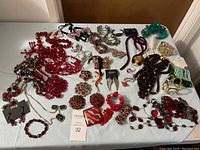 Top-down view of assorted costume jewelry on a white surface, showing predominantly red beaded necklaces, bracelets, brooches, earrings, and hair accessories.