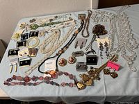 Photo showing full assortment of jewelry spread out including necklaces, earrings, bracelets, and brooches in various colors and styles
