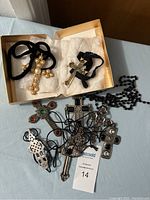 Box containing various cross necklaces including large pearl cross, metal crosses with decorative accents, and black beaded chain with cross pendant.