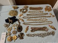 Full view of assorted gold-tone costume jewelry laid out on table including chains, brooches, pins, and bracelets.
