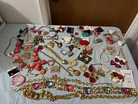Table layout featuring assorted heart-themed jewelry including earrings, necklaces, bracelets, and pins in gold, red, pink, and multicolor.