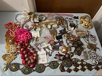 Top-down photo of a large assortment of costume jewelry including bead necklaces in bright pink, red, coral, brown; gold-tone bracelets; earrings on cards; rings; beaded decorative chains; brooches.