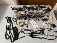 Multiple jewelry pieces spread on a white surface including necklaces, bracelets, earrings, and a large gold-tone cuff bracelet with a black stone