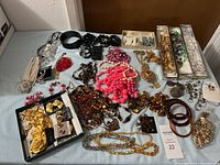 Full overhead shot of all assorted costume jewelry items on a blue surface showing necklaces, bracelets, earrings, and brooches in various colors and styles.