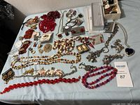 Wide view showing many assorted jewelry pieces spread on table including necklaces, earrings, pins, and a watches.
