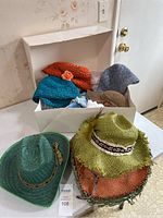 Photo shows all seven ladies summer hats in various colors arranged inside and around a white box on a chair.