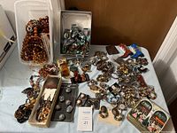 Photo showing assorted necklaces in brown and amber colors, earrings, bracelets, and brooches spread on table.