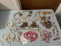 Overview of multiple pearl necklaces in white, pink, and bronze shades, gold-tone chain bracelets, and several earrings in small boxes.