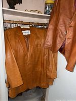 Two-button tan leather blazer hanging on rod with storage bins below