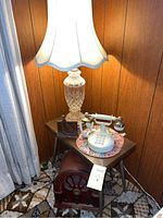 Photo of crystal table lamp with white shade, rotary phone, and vintage radio on a small side table.