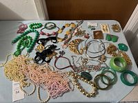 Full assortment of costume jewelry laid flat on a gray table showing various necklaces, bracelets, earrings, and pendants in different colors and styles.