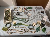 Overview of assorted jewelry laid out on a blue cloth, showing variety of necklaces, bracelets, earrings, and brooches mostly in green and silver tones