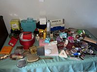 Full view of lot spread on table showing sample packets, mini bottles, boxed items, mirror, and brush