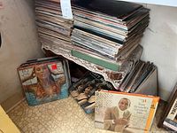 Two large stacks of vinyl LP records on a shelf with loose albums on the floor