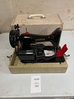 Full view of Spartan sewing machine threaded with red thread, powered by an attached motor, resting inside its carrying case.