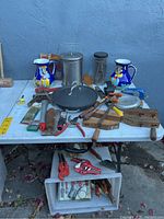 Full view of the lot on white table showing assortment of tools, cooking items, and decorative pitchers