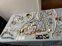 Wide view of the assortment of white themed costume jewelry including necklaces, bracelets, brooches, and earrings laid out on a table.