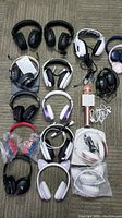 Overhead photo showing the full lot of 16 headphones in various colors and styles plus one rose gold karaoke microphone with square speaker and attached white cable.