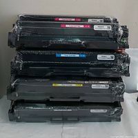 Stack of eight toner cartridges wrapped in plastic, showing the distinct color labels and form factor.