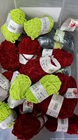 Mixed skeins of bright green and dark red Flower Alkdi yarn in a container