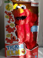 Front view of Playskool Friends Tickle Me Elmo plush toy in original open-front box showing red fur character with eyes and nose