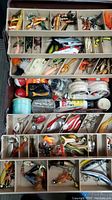 Top view of open three-tier tackle box with compartments showing mixed lures