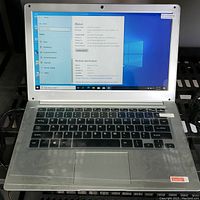 Open laptop displaying Windows 10 Pro About page showing system info on main desktop screen, silver chassis keyboard and trackpad visible.