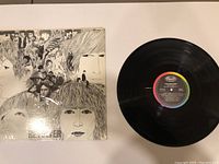 Photo showing The Beatles Revolver vinyl LP record next to its album cover featuring illustrated portraits of the band members.