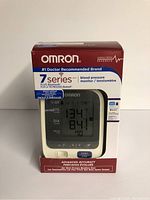 Photo of Omron 7 Series Bluetooth blood pressure monitor in its original box showing front of device and packaging details.