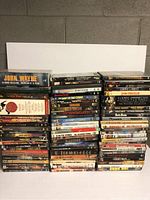 Large stack of assorted DVDs including box sets and multiple single movie titles, arranged in three main vertical stacks with titles visible on spines.