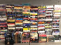 Wide shot showing tall stacks of numerous VHS tapes arranged together, mixed titles and multiple boxed sets visible.