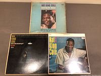 Three Nat King Cole vinyl album covers and records, showing wear on edges and discoloration on covers.
