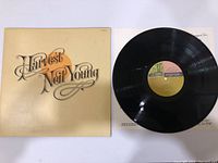 Photo showing front album cover with Harvest Neil Young text and vinyl disc placed partly on cover