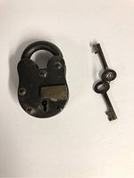 Front view of antique prison lock with shackle and one key beside it showing lock keyhole and surface details