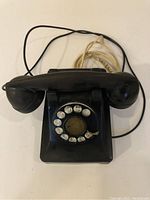 Full view of black rotary dial telephone with handset and cords, showing overall condition and design.