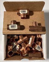 Photo showing an open box with 15 copper tee fittings inside, each 1/2 inch in diameter, with some fittings placed on top of the box.