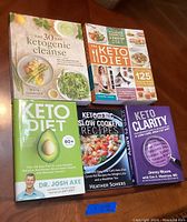 Photo showing 5 keto diet books with visible titles and authors, arranged on a wooden surface.